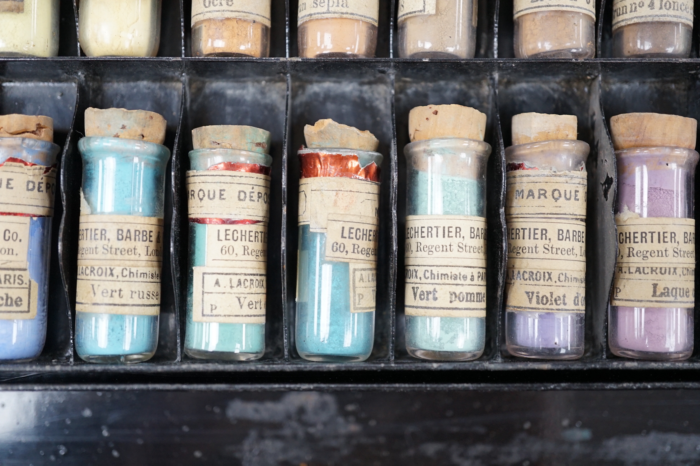 A black artist's tin box, with fitted interior, containing glass phialls of coloured shades of powdered paint and a white glass samples panel etc, box 37.5cm wide, 27cm deep